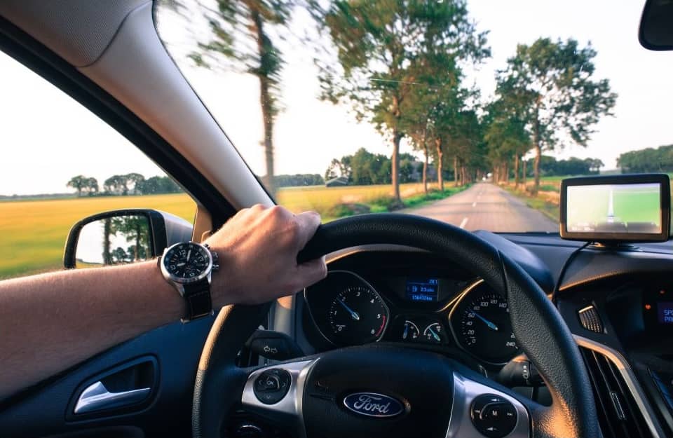 A man driving a sedan down a sunny road.
