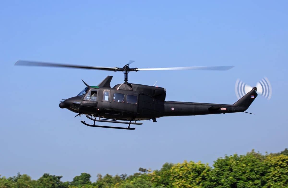 A black helicopter hovering over green trees.