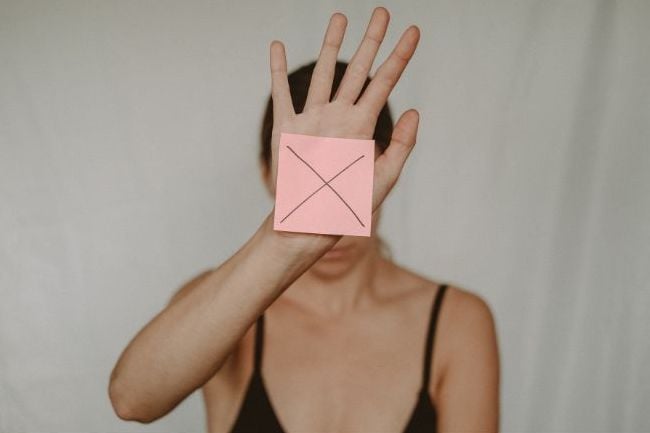A woman holding a card over her face with a big X on it.