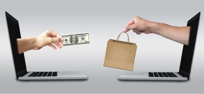 A hand holding a $100 bill and another hand holding a bag.