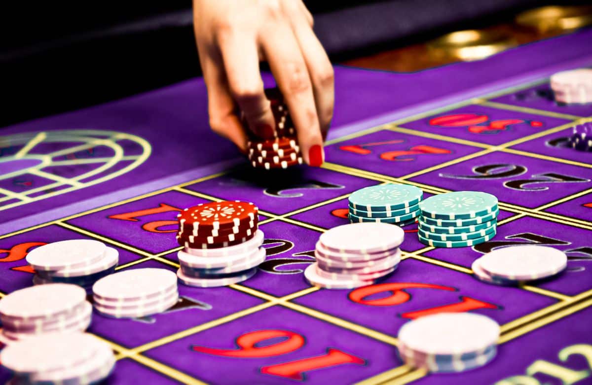 A hand stacking $5 chips on a purple roulette table in a casino.