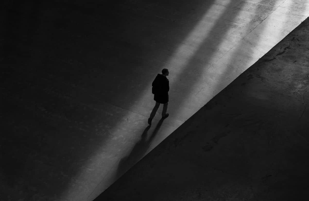 A man walking on a dark pathway and casting a shadow.